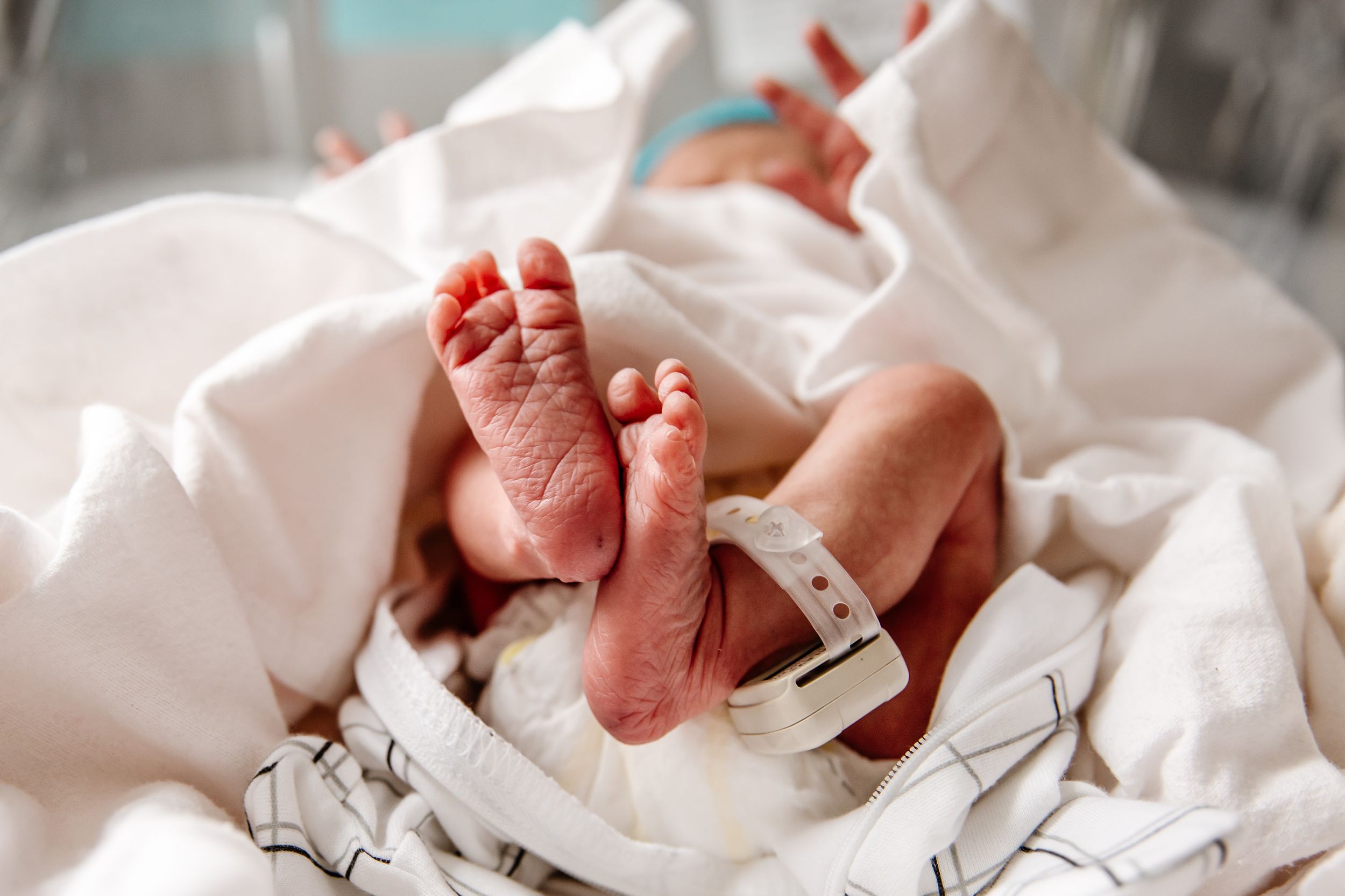 Newborn baby feet with hospital bracelet wrapped in white blanket in delivery room.
