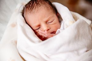 Peaceful newborn baby swaddled in white blanket with eyes closed sleeping.
