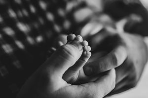 Black and white close-up of a newborn baby's tiny feet cradled in an adult's hands.