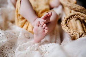 Newborn baby feet resting on white lace fabric beside a wicker basket in warm tones.