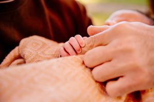 Newborn baby grasping parents finger wrapped in soft orange blanket closeup.