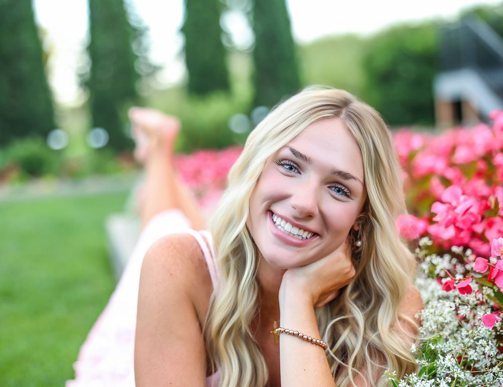 Outdoor portrait among pink flowers with natural smile and flowing hair.