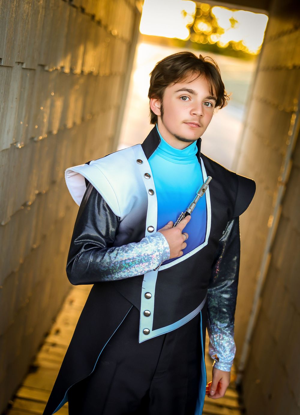 Person wearing formal black suit and blue sash poses in dramatic indoor lighting.