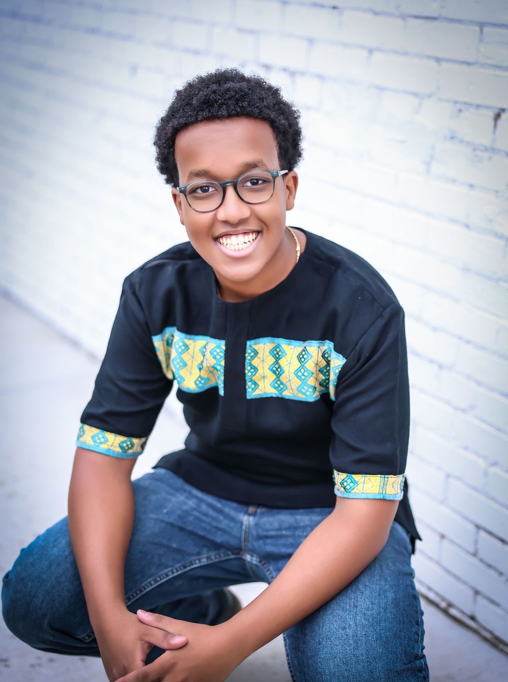 Casual portraits featuring black shirt with decorative teal trim against white brick wall.