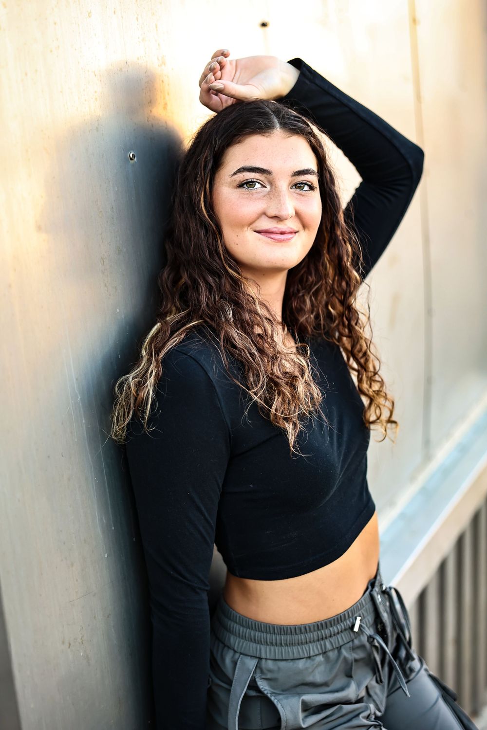 A sequence of poses in a black crop top and gray shorts against a light colored wall.