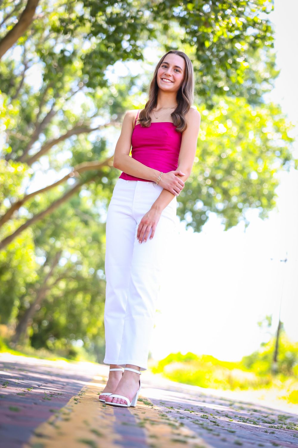 Summer outdoor photoshoot featuring pink top and white pants against natural foliage.