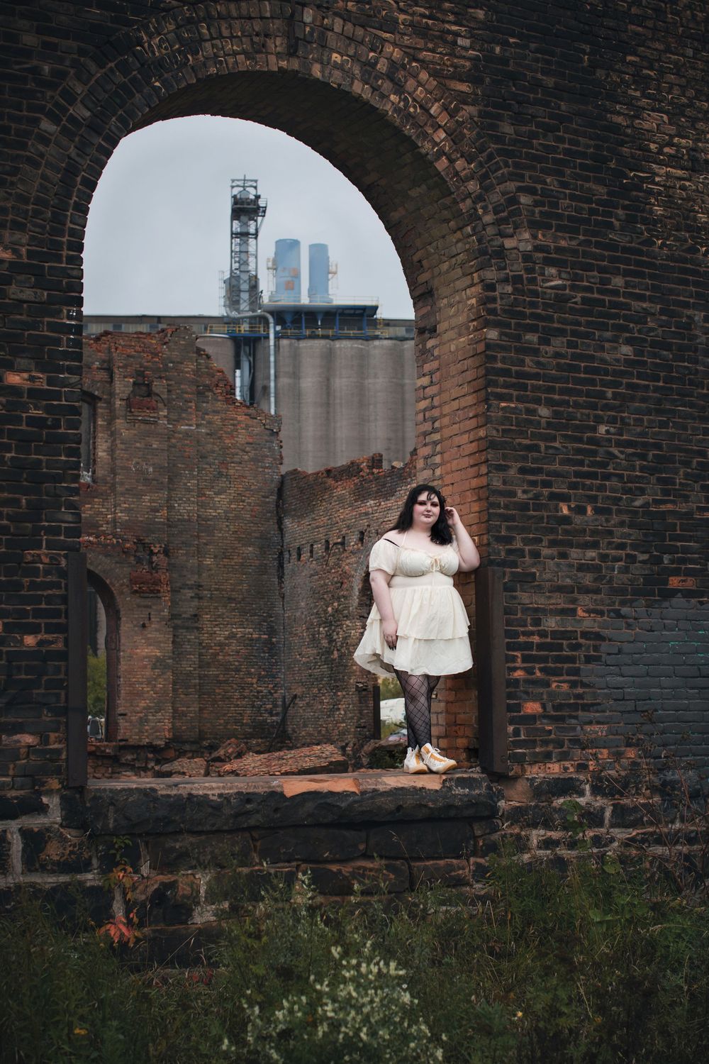 A sequence of arched brick windows frames an industrial scene with grain silos in the background.