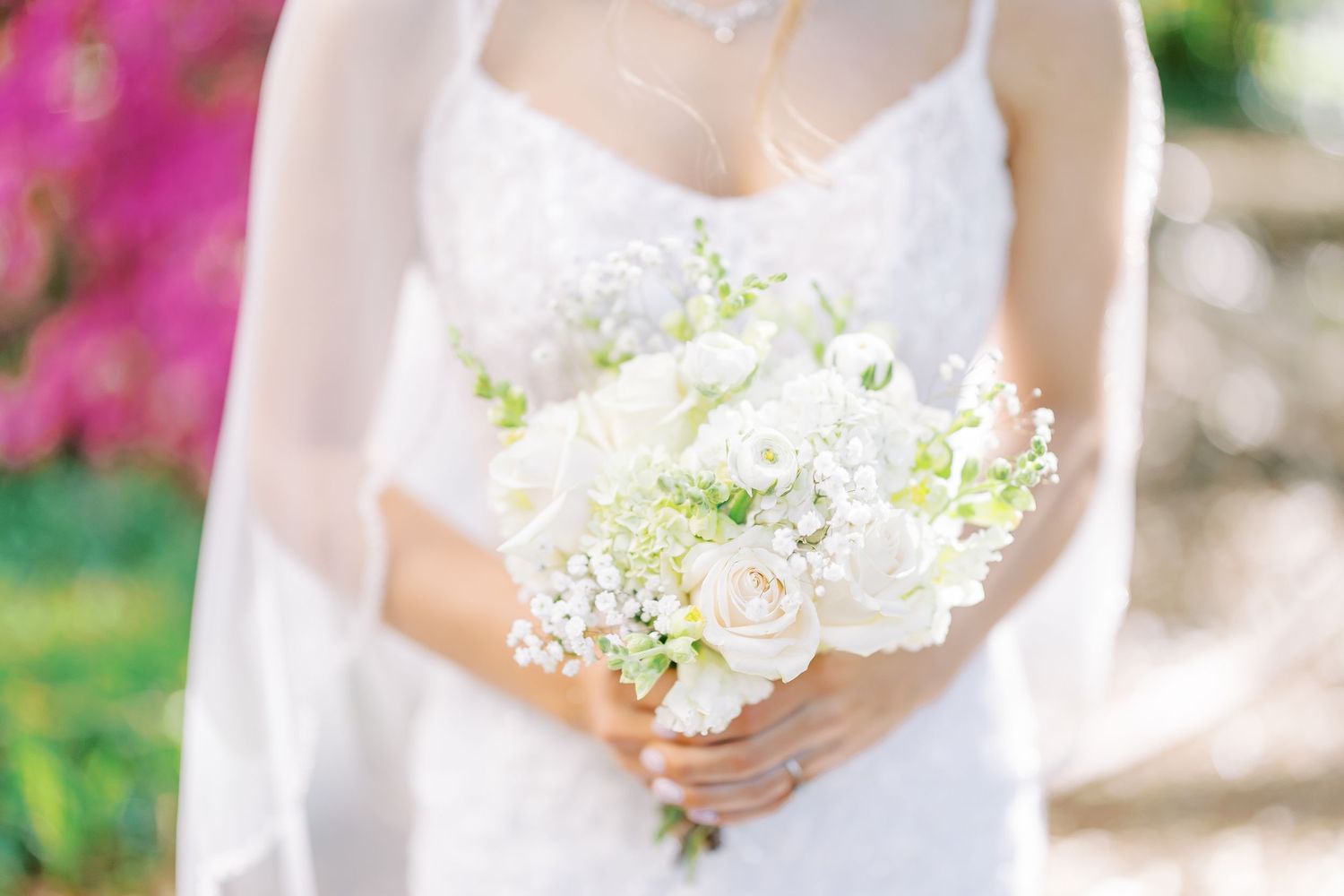 A bride in a white wedding dress holds a delicate bouquet of baby's breath flowers against a soft blurred background.