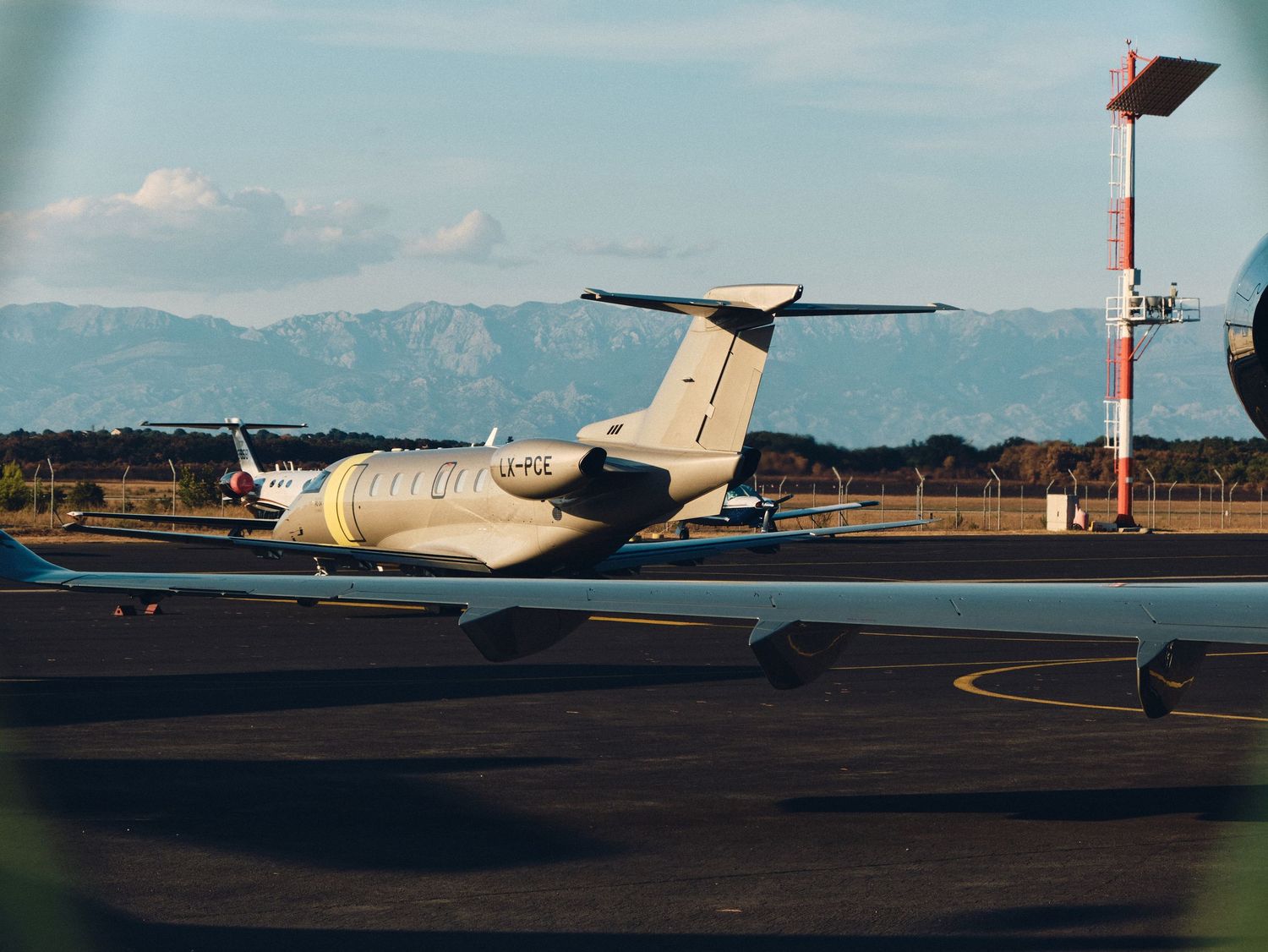 Private jet aircraft parked on tarmac with mountains and air traffic control tower visible in background.