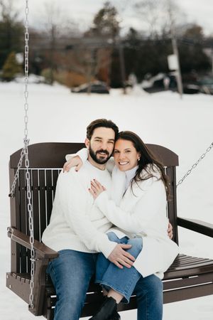 A couple shares tender moments on a wooden porch swing during a snowy winter day.