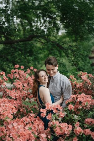 A couple shares intimate moments among blooming coral-colored azalea bushes in a lush garden setting.