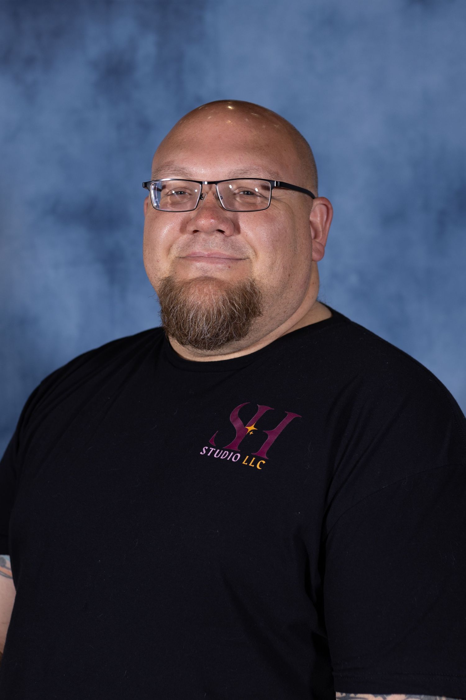 Professional headshot of person in black t-shirt with company logo against blue mottled background.
