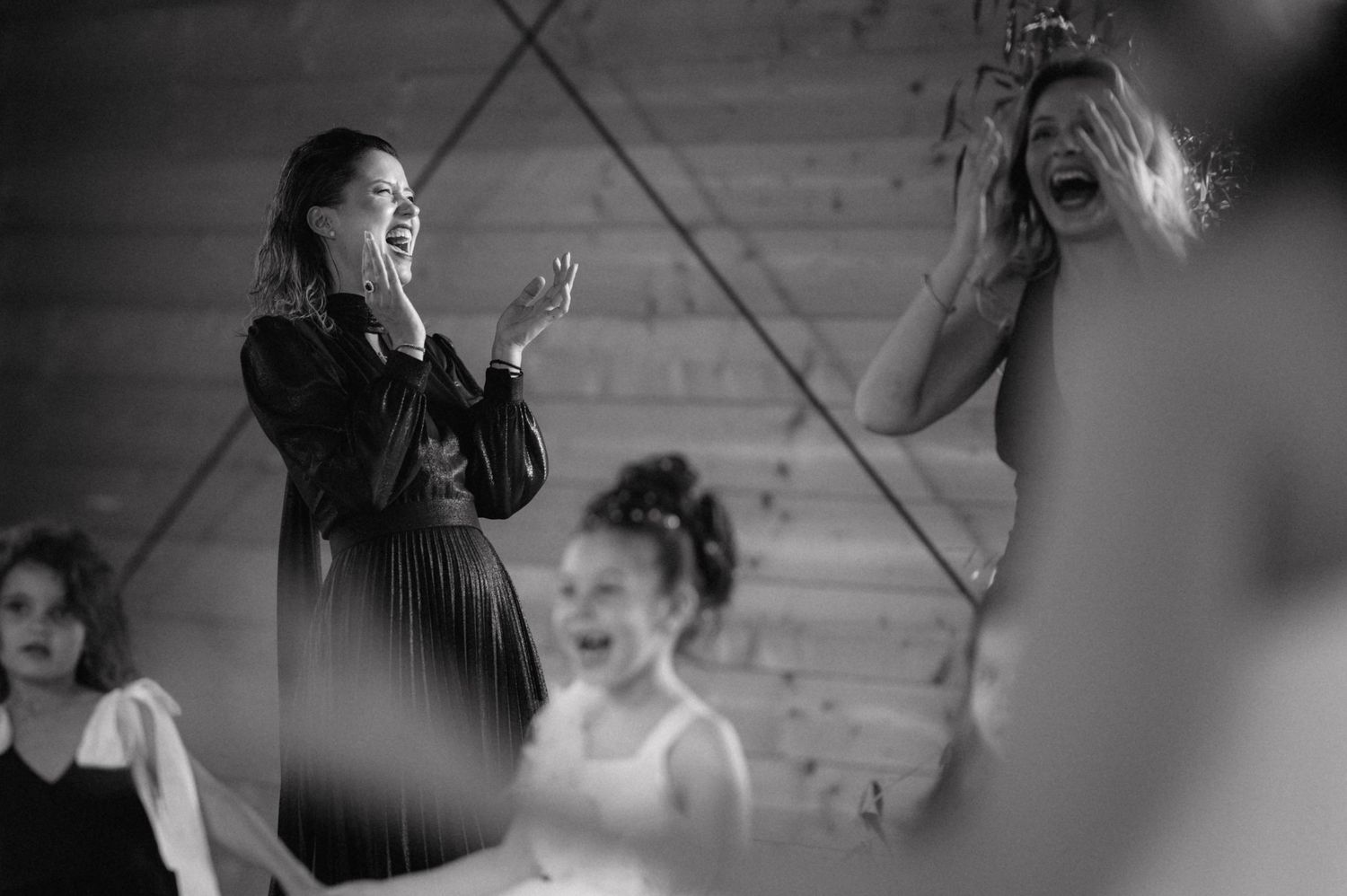 Black and white candid photo of emotional reactions and laughter during a joyful wedding reception moment.