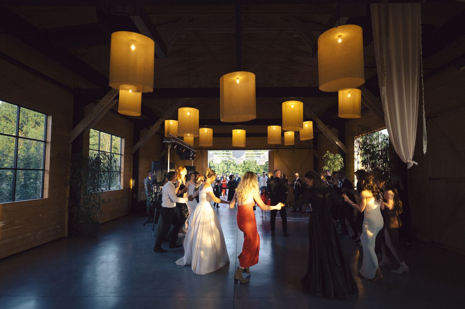Wedding guests dance under glowing lantern lights in an elegant reception venue with floor to ceiling windows.