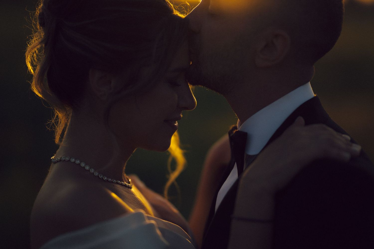 A romantic silhouette of a couple in formal attire illuminated by warm golden backlighting at sunset.