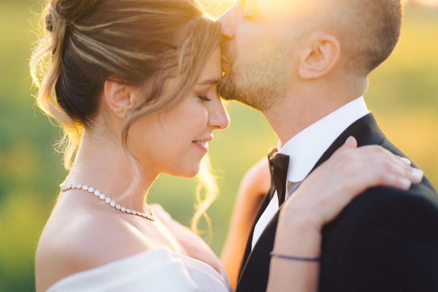 Romantic sunset photo of newlyweds in formal attire sharing an intimate moment in golden light.