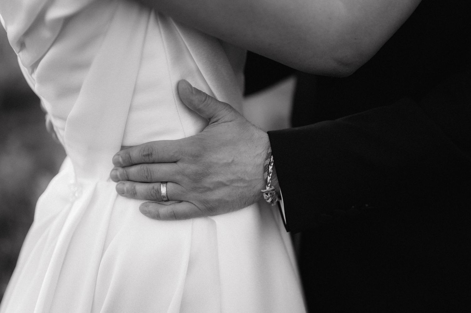 Close-up black and white shot of hands embracing at a formal event.