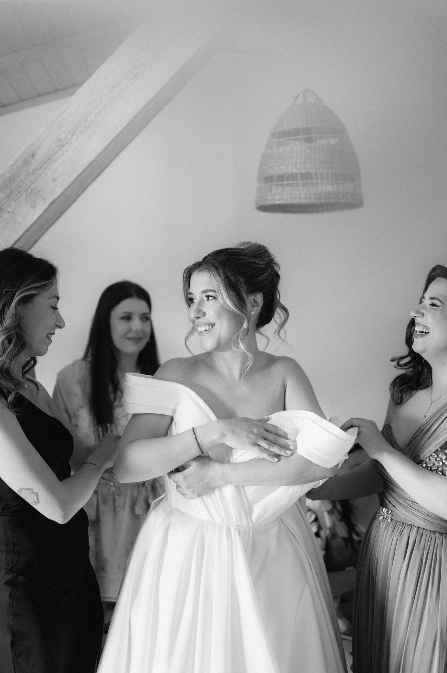A candid black and white photo showing bridesmaids helping with final wedding dress preparations.
