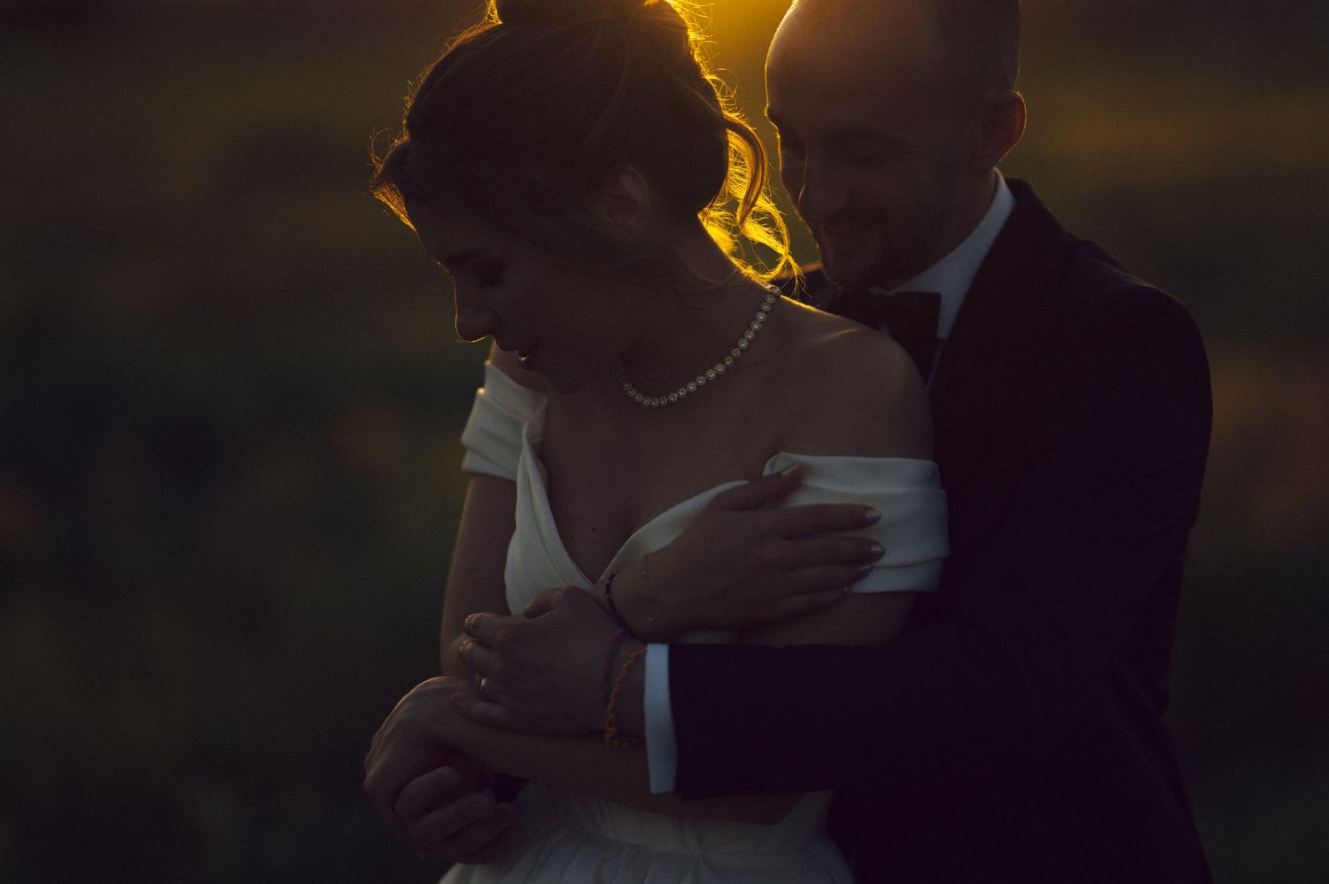 A romantic silhouette of a couple in wedding attire embracing at sunset with a golden backlit glow.