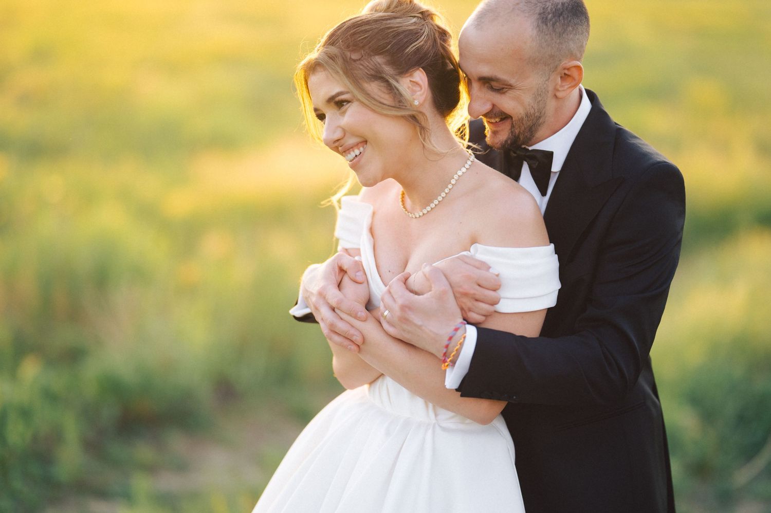 A joyful couple embraces in a sunlit field during their wedding photoshoot at golden hour.