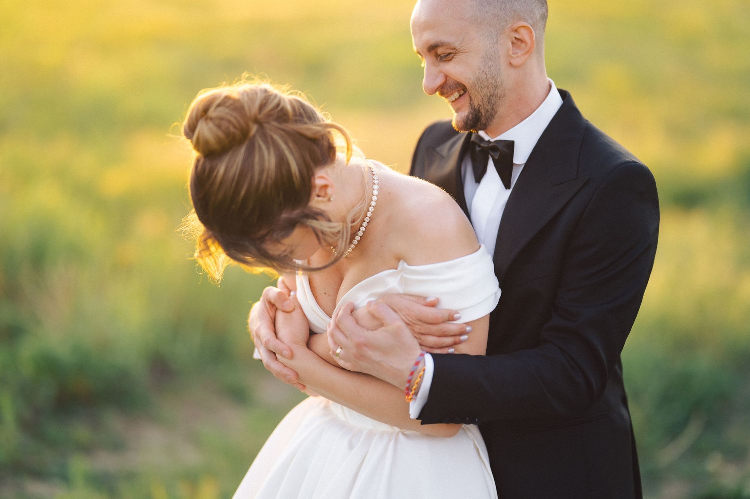 A joyful couple shares a romantic moment in their wedding attire against a soft golden sunset background.