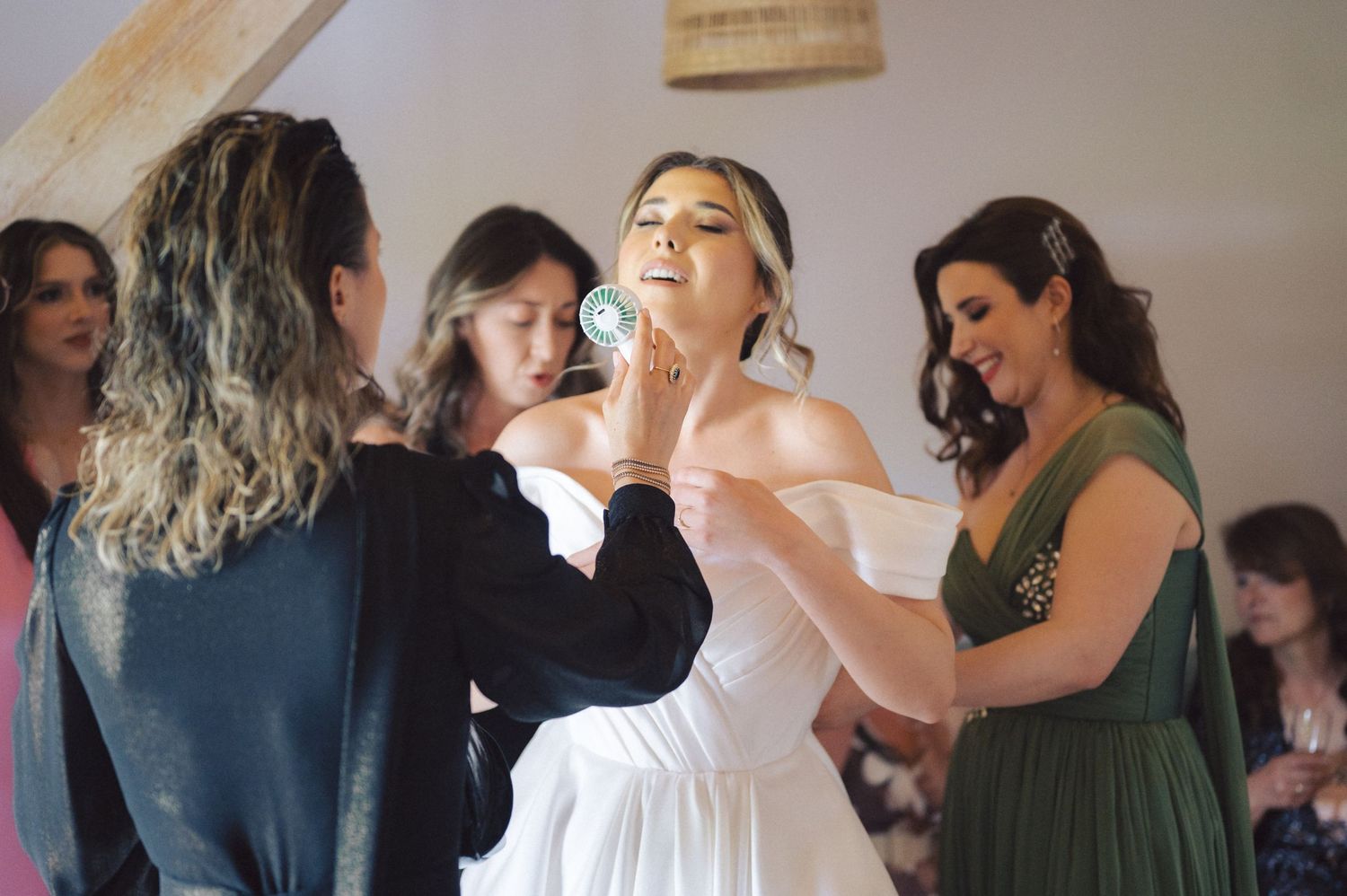 Wedding preparations underway as a bride gets makeup applied while wearing a white dress with bridesmaids in green nearby.