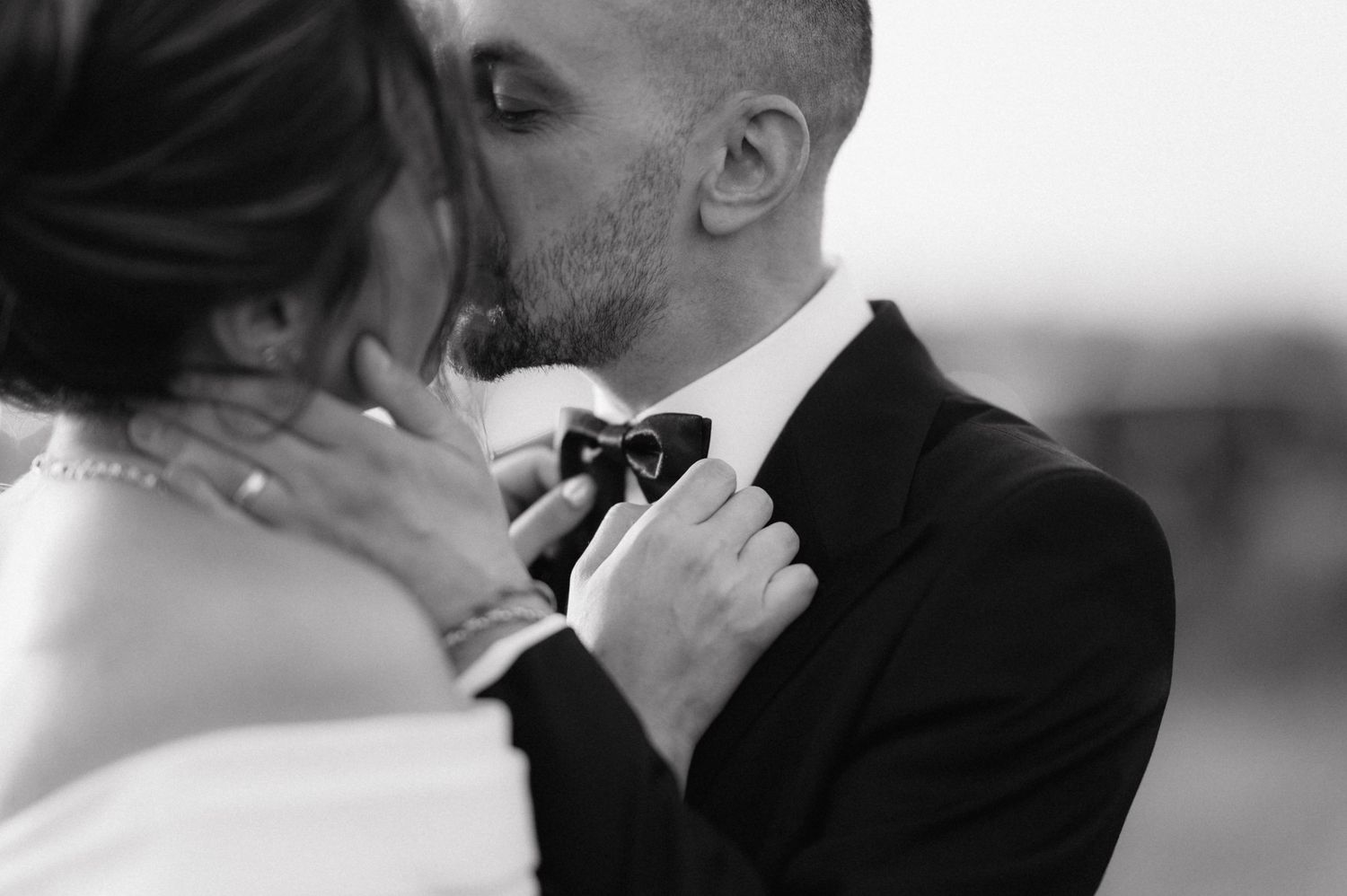 An intimate black and white wedding photo of a couple sharing a tender moment while the bride adjusts the groom's bowtie.