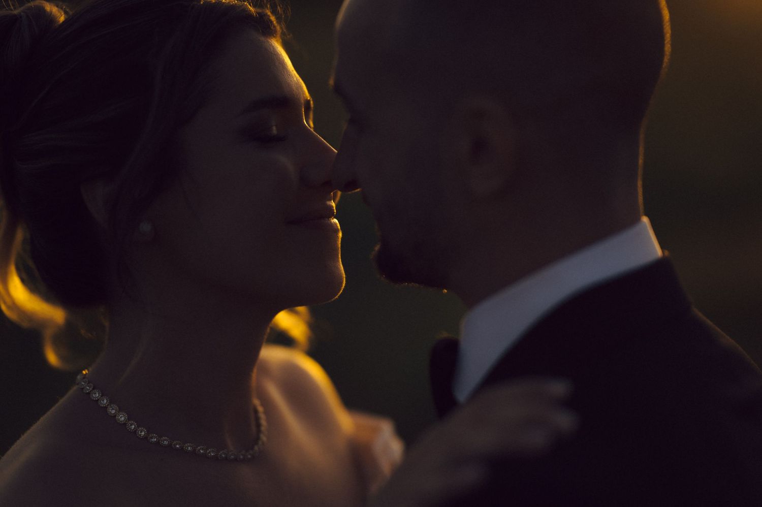 A close-up silhouette shot of a romantic couple during a wedding dance, with warm backlighting creating an intimate mood.