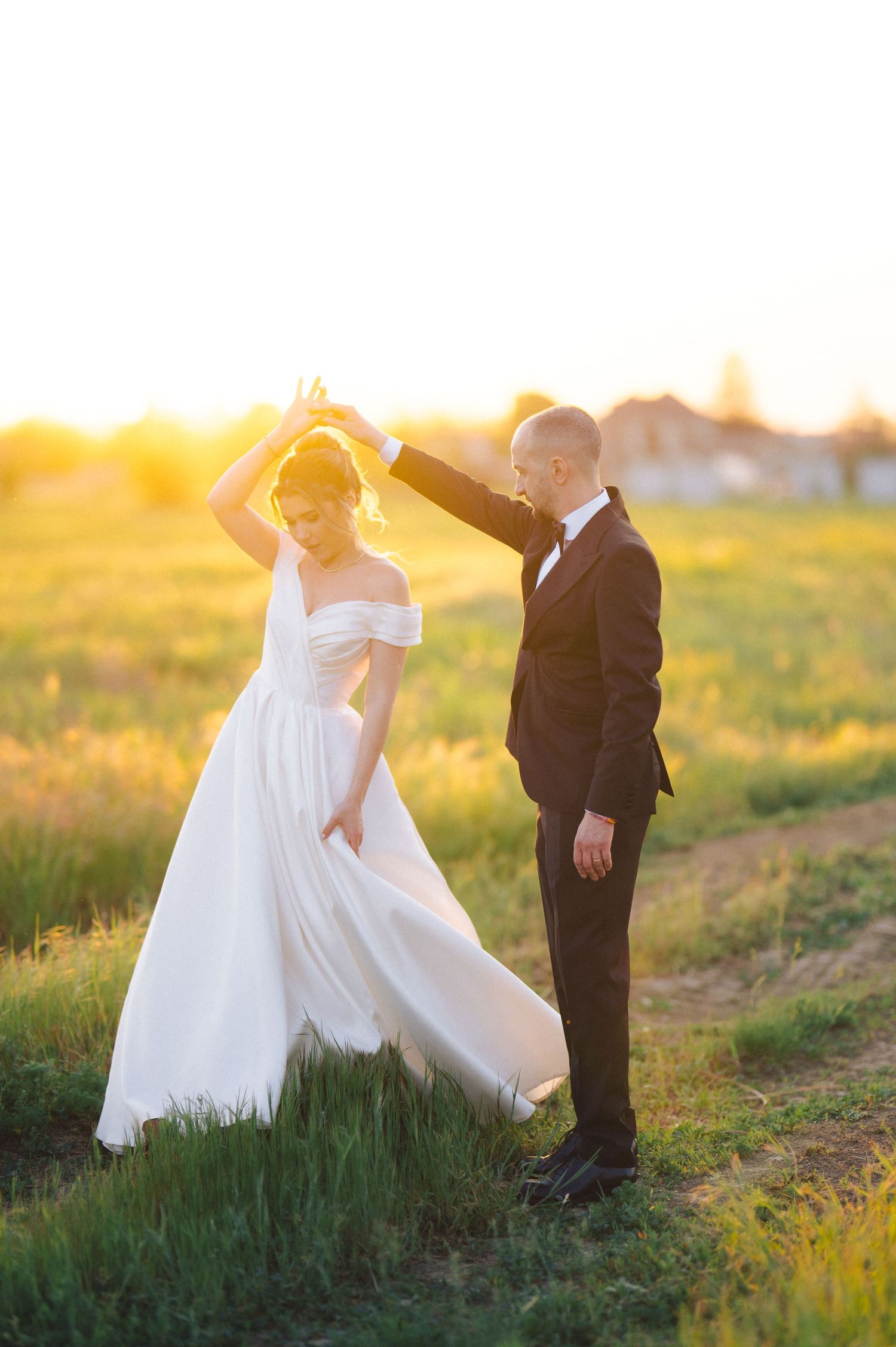 A romantic sunset wedding photo with the bride in a flowing white gown dancing while the groom leads in a dark suit.