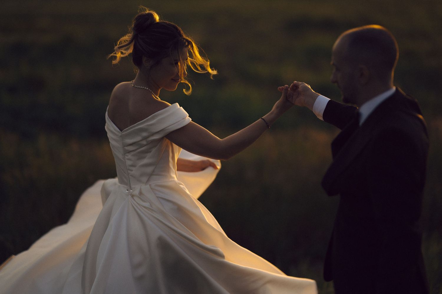 A couple dances together at sunset, with the bride's white dress flowing elegantly in the golden light.
