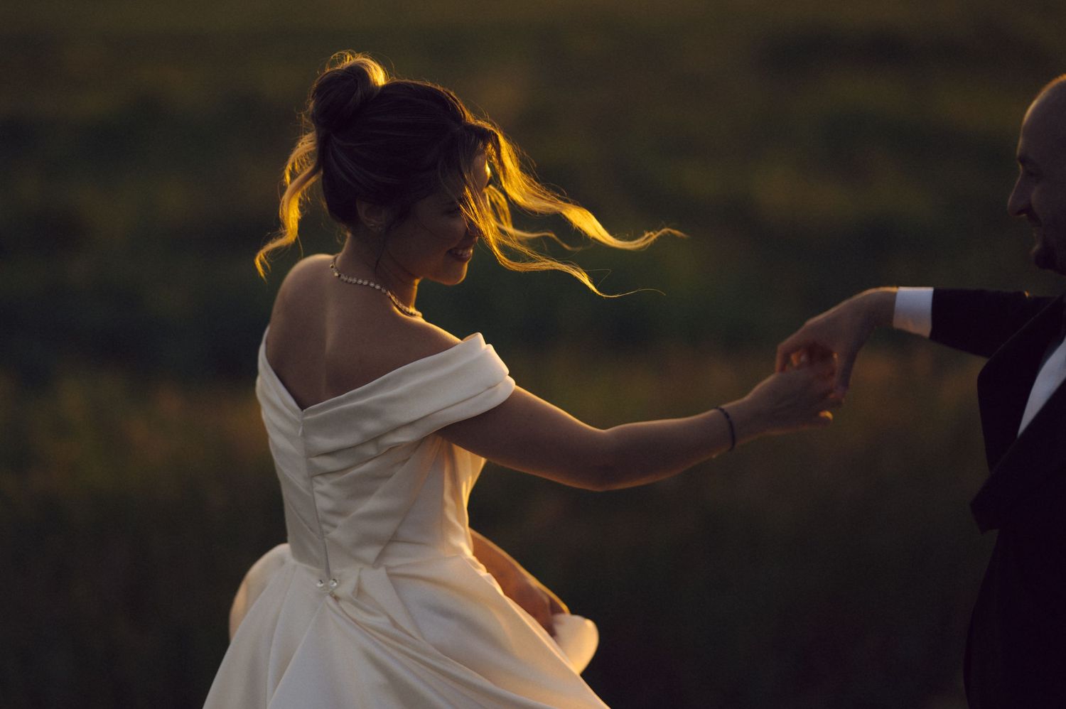 A bride in a flowing white dress dances at sunset, her hair catching the golden light as her dress twirls around her.