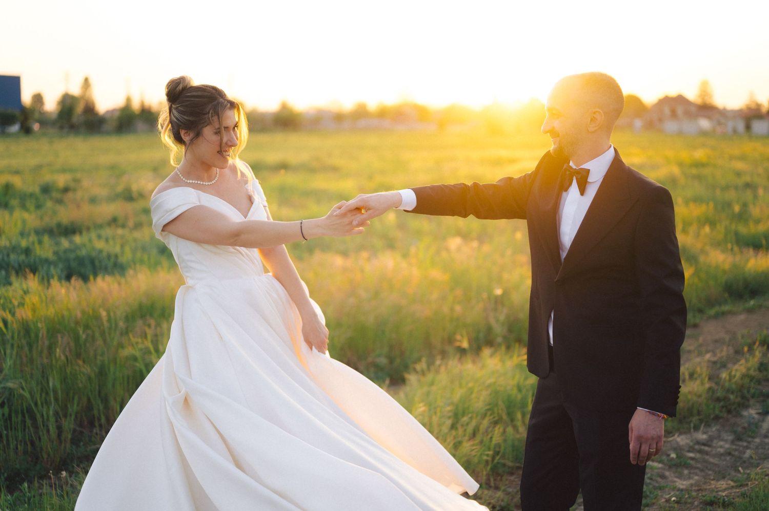 A bride and groom dance in a golden field at sunset creating a romantic silhouette.