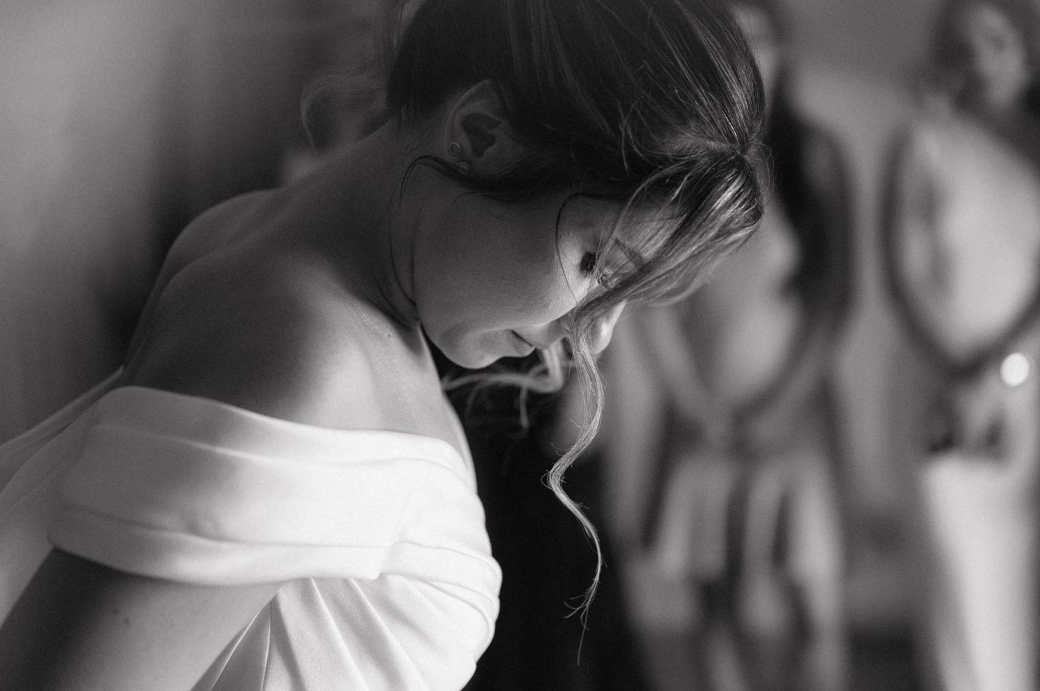 Black and white portrait of a person with head bowed, wearing an off-shoulder white top.