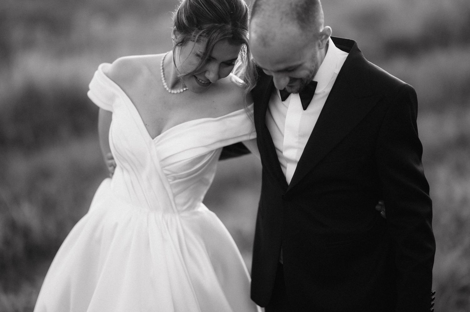 A black and white wedding portrait shows a couple in formal attire sharing an intimate moment outdoors.
