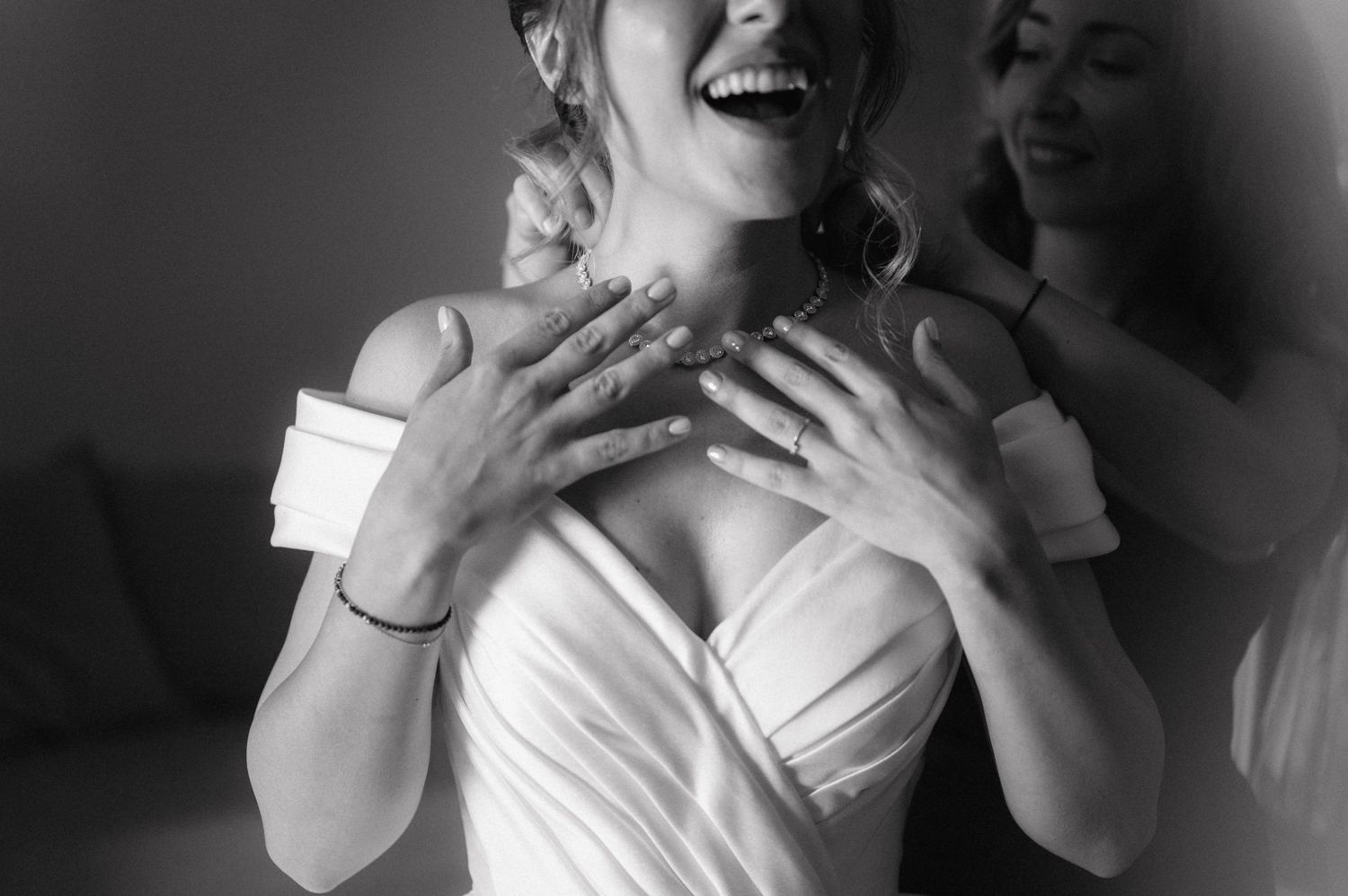 Black and white photo of a joyful bride laughing and holding her hands to her chest in an emotional candid moment.