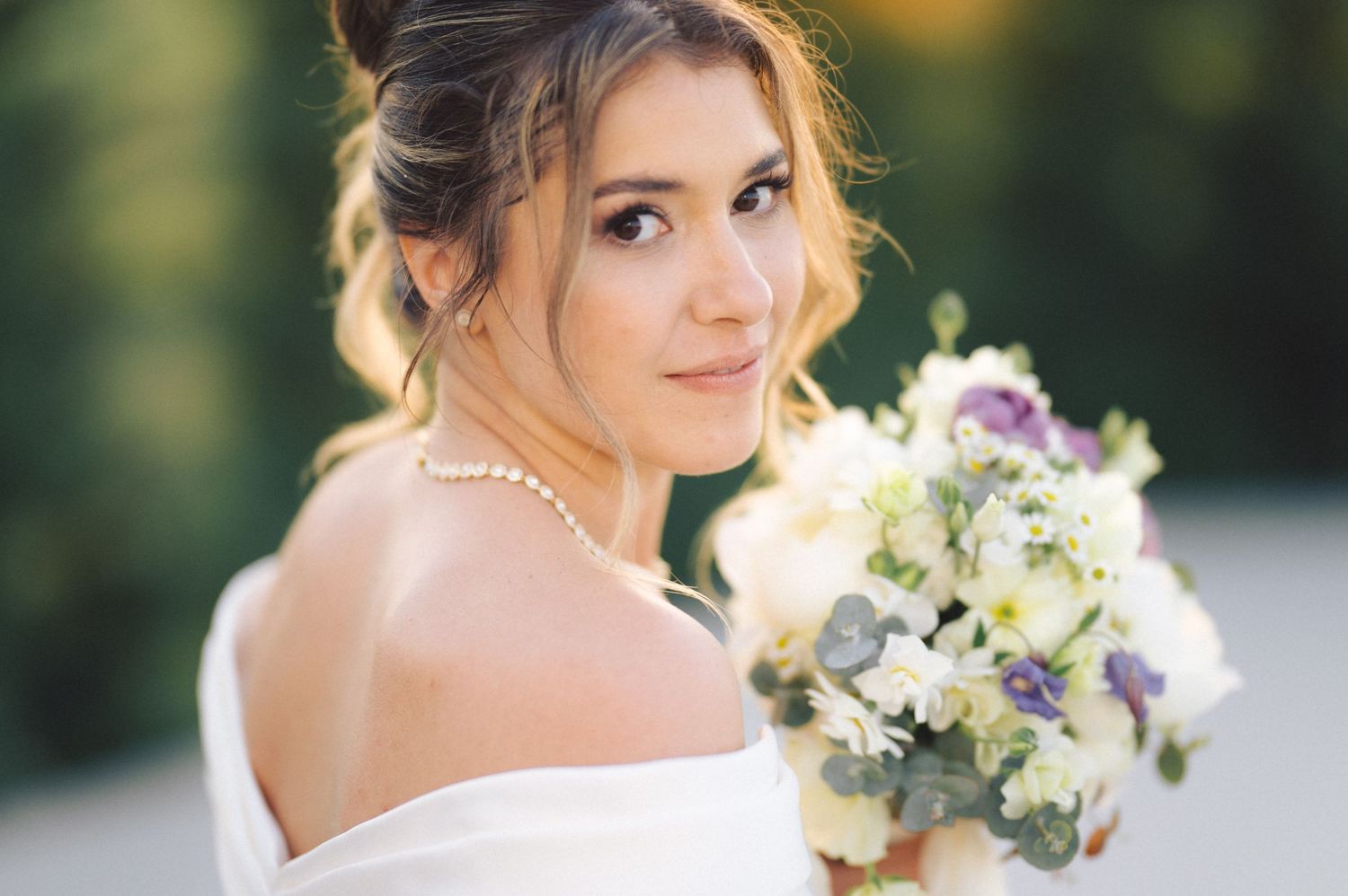 Classic bridal portrait featuring an off-shoulder white dress and delicate floral bouquet.