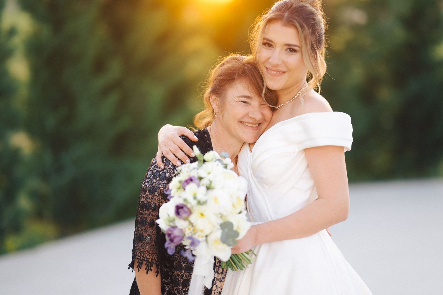 Sweet embrace between bride in white dress and companion during sunset wedding photoshoot.