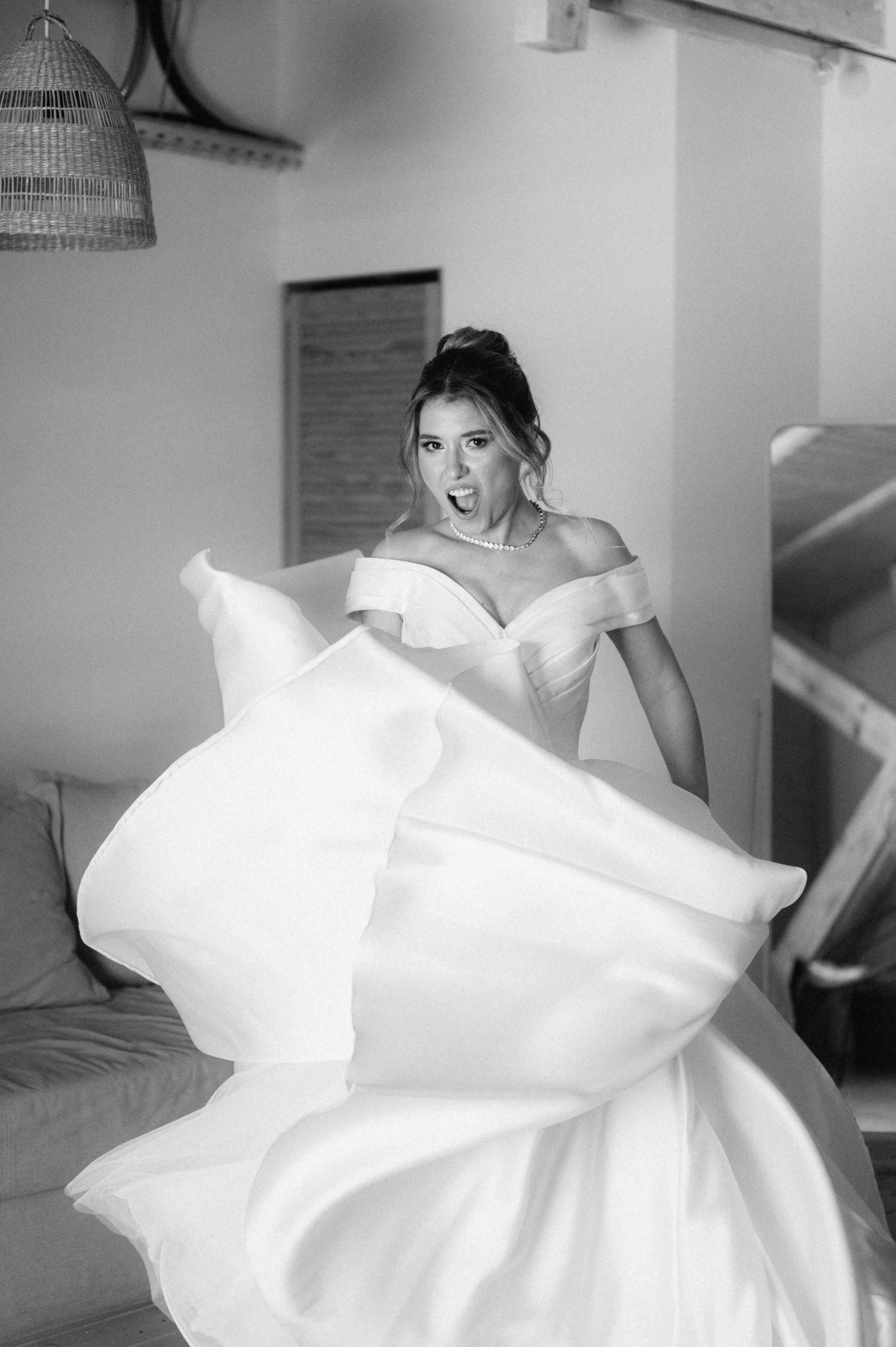 Black and white photo of a bride in an off-shoulder wedding dress with flowing fabric in motion.