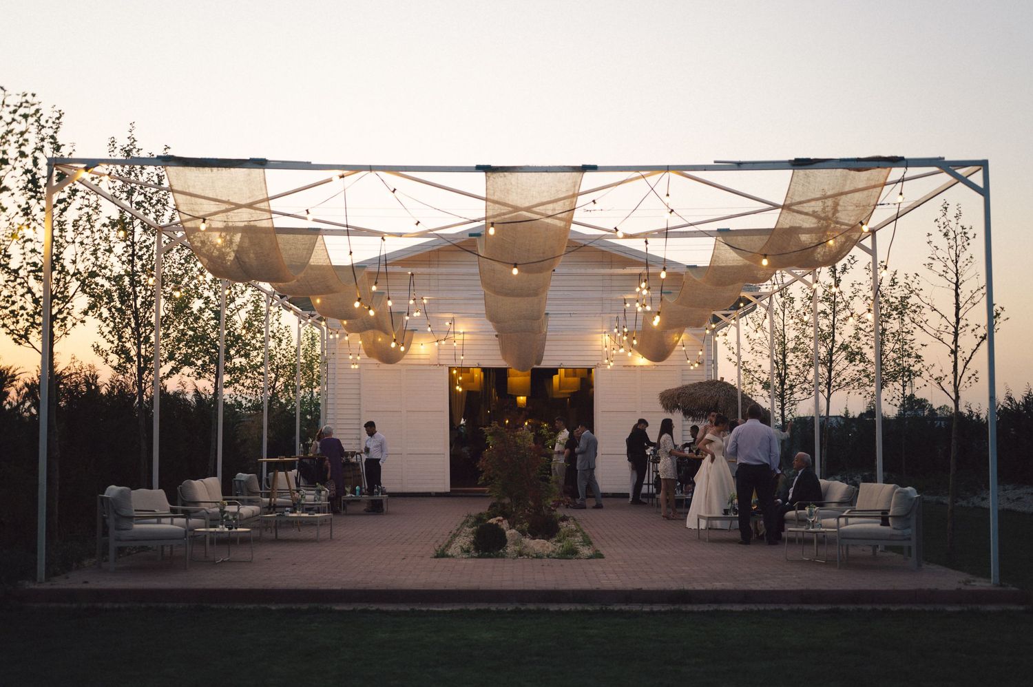 An outdoor event space with modern white canopy and seating at sunset features guests enjoying the evening atmosphere.