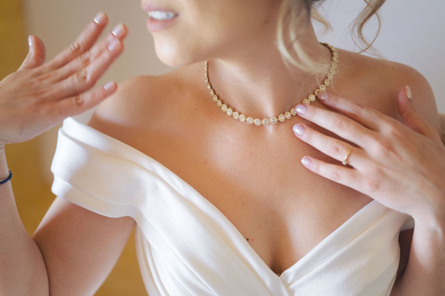 Close-up of bride wearing pearl necklace and white off-shoulder wedding dress showing delicate hand gestures.