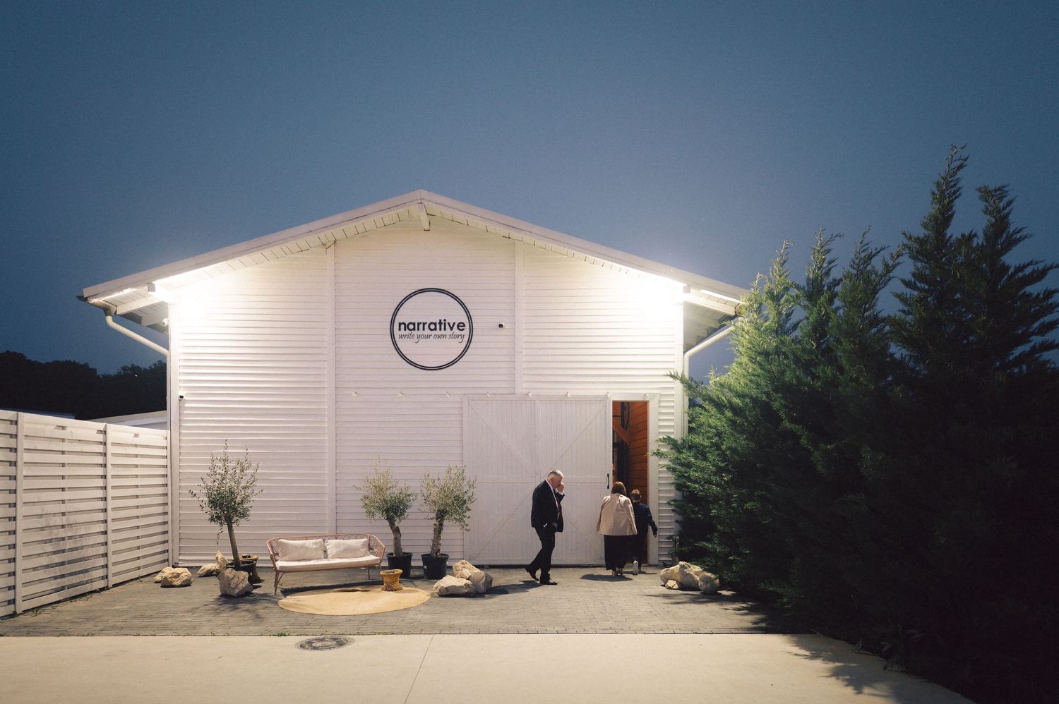 A small white modern building with a circular logo and person standing outside at dusk.