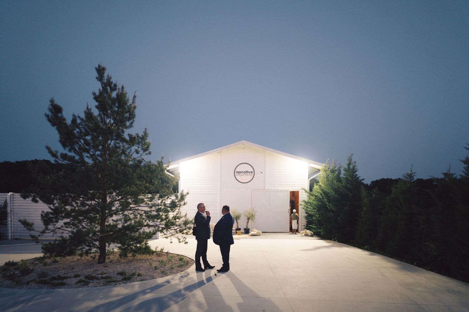 A silhouetted couple stands in front of an illuminated white building at dusk.