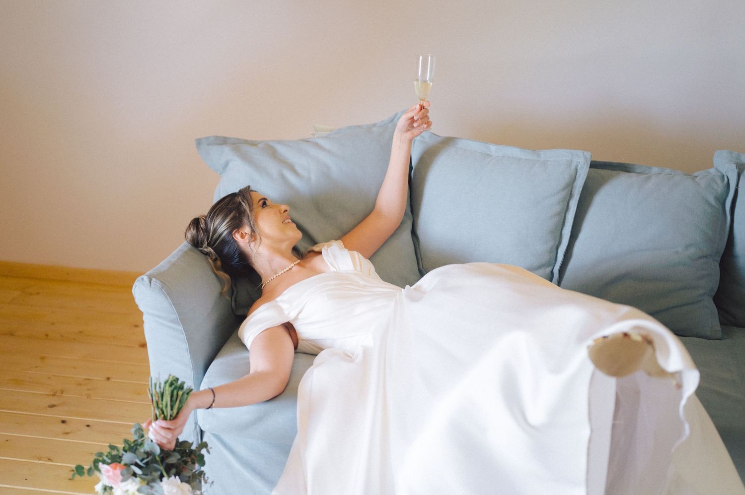 A person in a white dress reclines on a light blue couch with a small floral arrangement nearby.