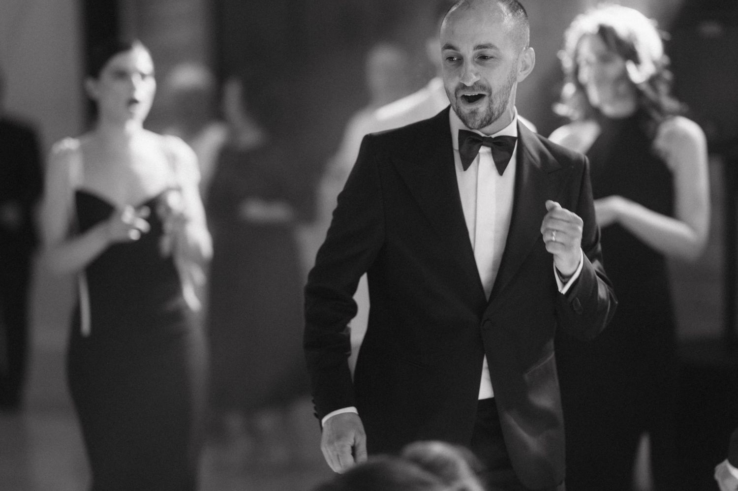 A black and white photo shows people dressed formally at an elegant evening event.