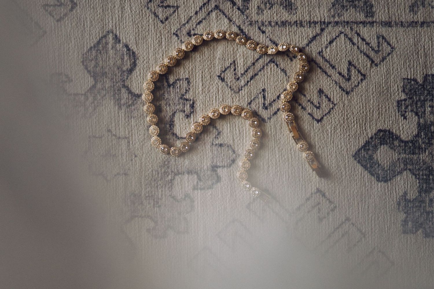 A delicate pearl necklace arranged in a curved shape on a textured gray background with geometric patterns.