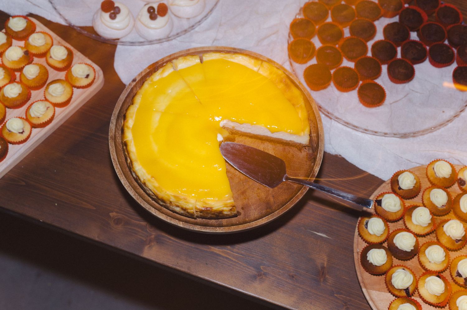 A bright yellow lemon tart with a slice cut out sits among platters of cream-filled pastries and chocolate truffles.