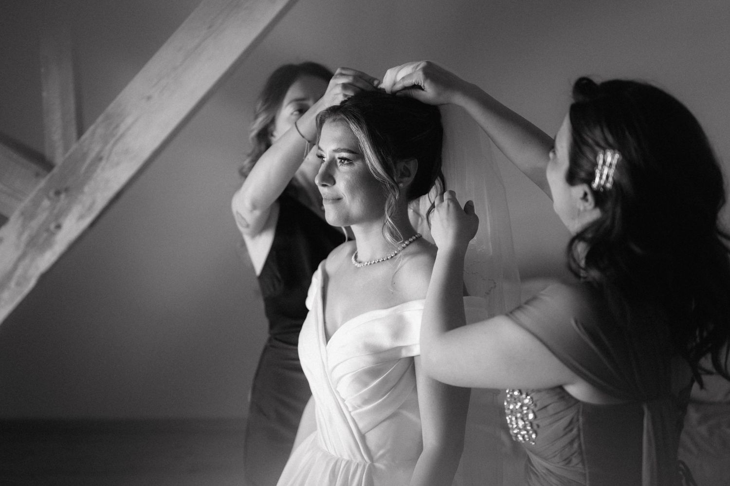Black and white photo showing preparations before a wedding as people help adjust a white bridal gown.