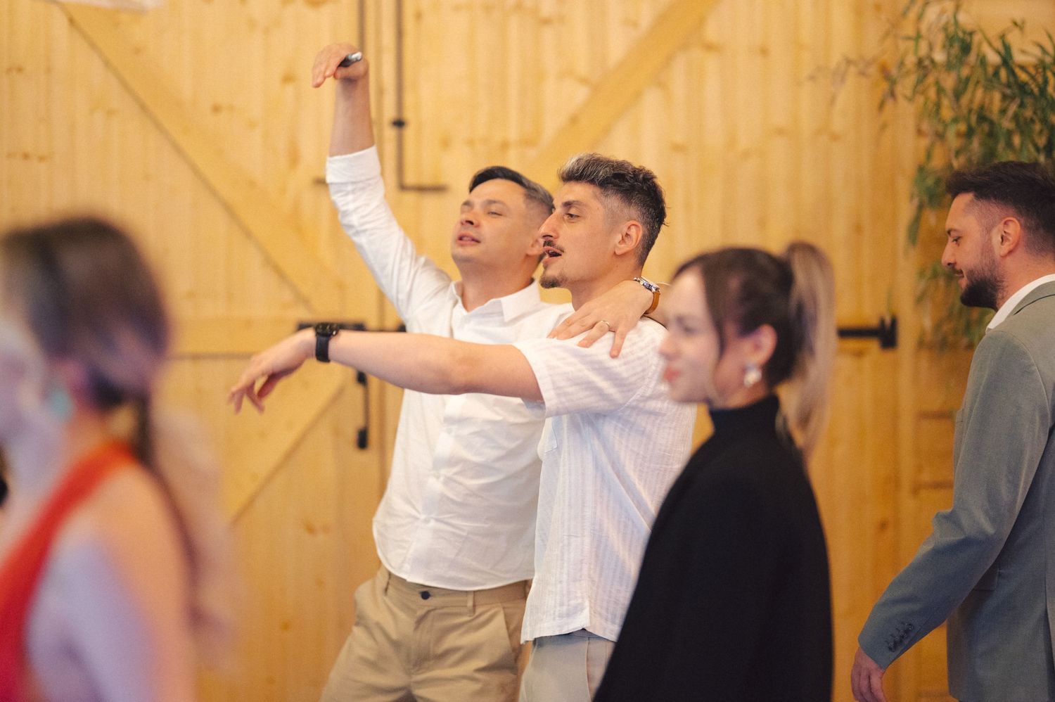 Energetic crowd at a social gathering with people dancing and celebrating in a wooden-paneled venue.
