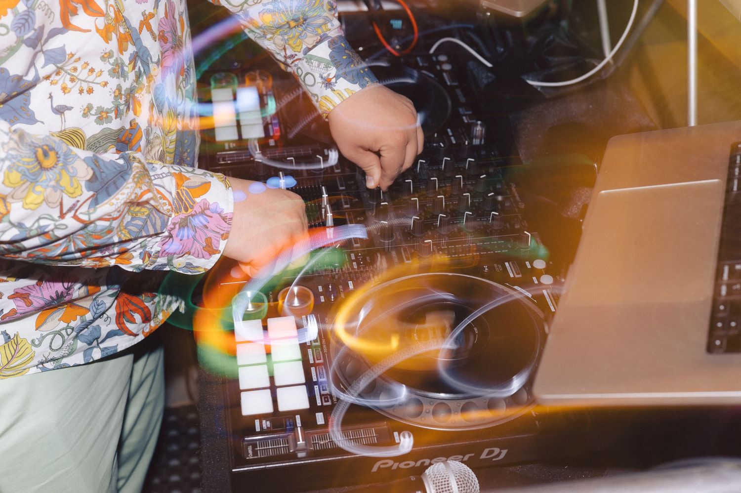 DJ performs on digital mixer equipment with colorful lighting effects at a music event.