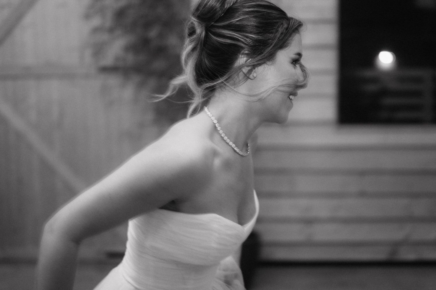 A person in a strapless white dress captured in an artistic black and white photograph with a candid expression.
